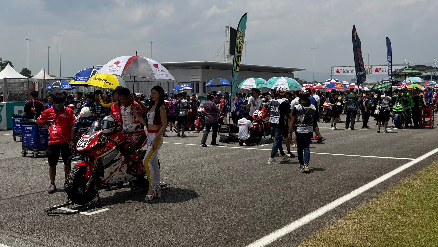 People gathered around a motorcycle on a race track with tents and buildings in the background.